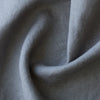 A close-up of draped light gray linen fabric showing its natural woven texture and soft folds.