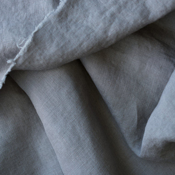 A close-up of draped light gray linen fabric with a visible woven texture and slightly frayed edge.