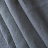 A close-up of draped gray fabric with a visible woven texture, arranged in soft diagonal folds.