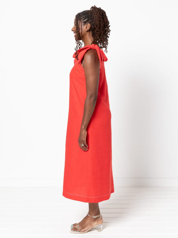 Woman wearing a red dressmade using a style arc Esther woven dress sewing patternwith bow straps on a white background