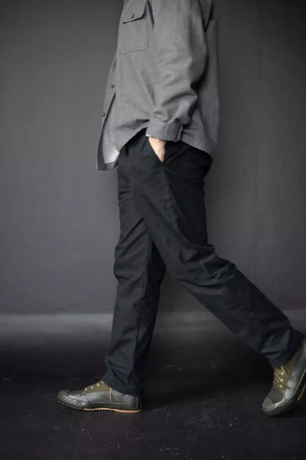 Person wearing a gray shirt and black pants against a dark background