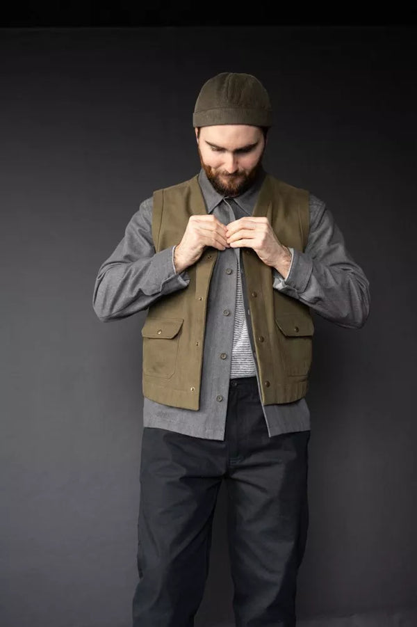 Man wearing a green vest over a gray shirt with a dark background