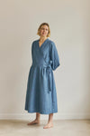 Woman wearing a blue malie Wrap Dress made with PDF sewing pattern against a plain background