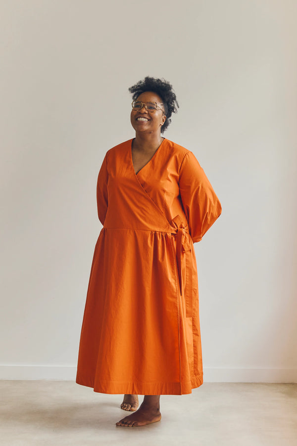 Woman wearing an orange malie Wrap Dress made with PDF sewing patternstanding against a plain background
