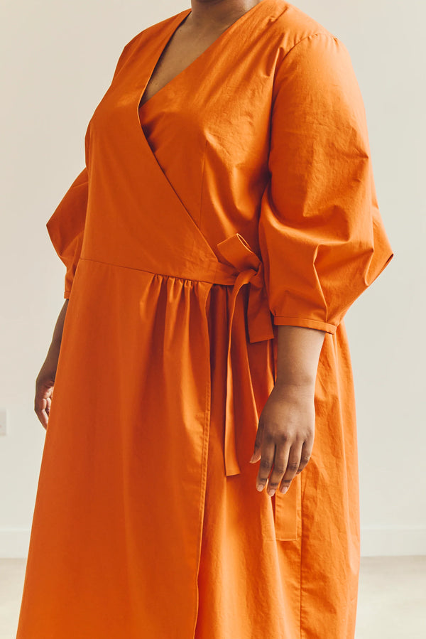 Person wearing an orange malie Wrap Dress made with PDF sewing patternagainst a plain background