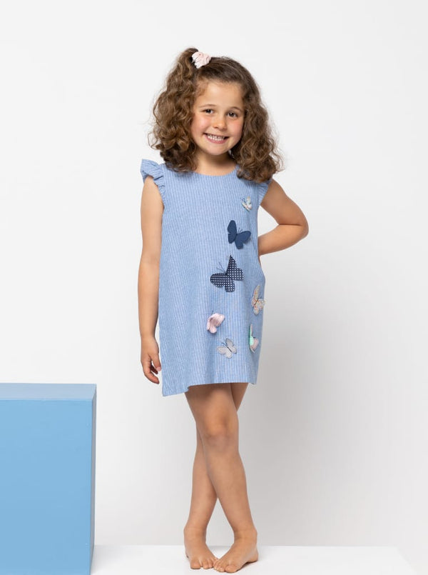 Young girl wearing a blue dress made using andie kids dress sewing patternon a white background