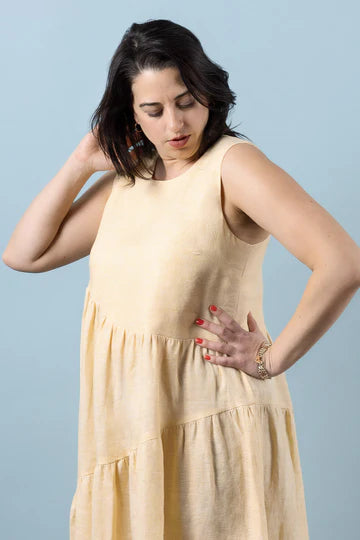 Woman wearing a beige dress made using Azure Dress, Skirt, and Top sewing pattern against a light blue background