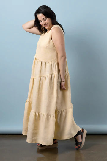 Woman wearing a long beige dress made using Azure Dress, Skirt, and Top sewing pattern against a light blue background
