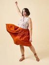 Woman wearing a floral top and orange skirt made using Azure Dress, Skirt, and Top sewing pattern on a beige background
