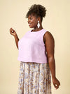 Woman wearing a light purple sleeveless top and floral skirtagainst a beige background
