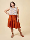 Woman wearing a floral top and rust-colored skirt on a beige background