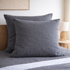 Two Charcoal grey European linen pillows on a bed with a neutral background