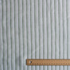 Coastal Sage Stripe linen fabric with soft sage-green and white yarn-dyed stripes, 100% linen, 130 GSM, 60 LEA with a ruler for scale on a white background