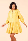 Woman wearing a yellow Poppy Dress with long sleeves on a beige background
