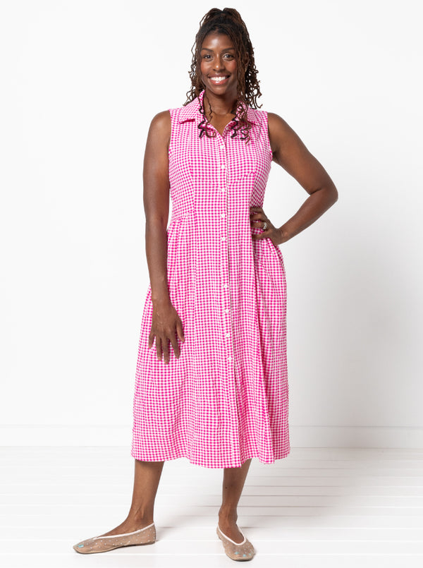 Woman wearing a pink checkered dress on a white backgroundThe dress is made from the Hampton Woven Dress Sewing Pattern – a mid-calf shirtdress with a gathered skirt, curved waist, sleeve or sleeveless options, and inseam pockets.