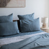 Blue bedding set on a bed with a lamp and painting in the background