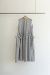 A sleeveless gray and white textured dress with side tie details, hanging on a wooden hanger from a wooden clothing rack against a plain white wall.