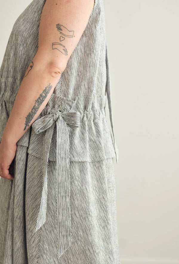 Close-up of a person wearing a sleeveless, textured gray and white striped dress with a tied waist sash, set against a plain light background.