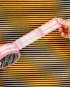 Hand holding a pink and white striped object against a yellow and black striped background