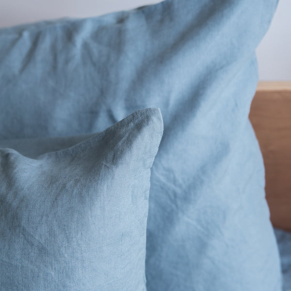 Close-up of a Lake Blue 100% Linen European Pillowcase and blanket on a neutral background