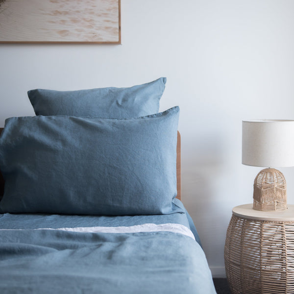 Lake Blue flat sheet 100% linen on a bed with a lamp and side table in the background.