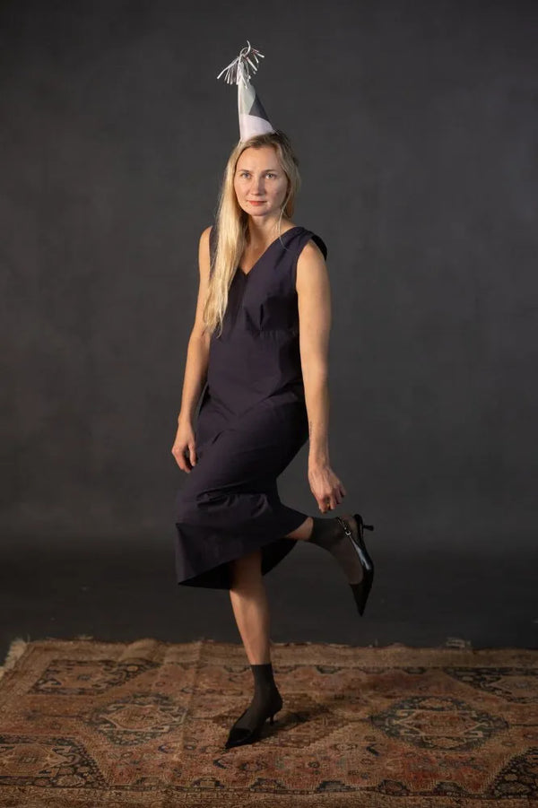 Woman in a dark dress made using The Lilian Sewing Pattern by Merchant & Mills with a cone-shaped hat on a dark background