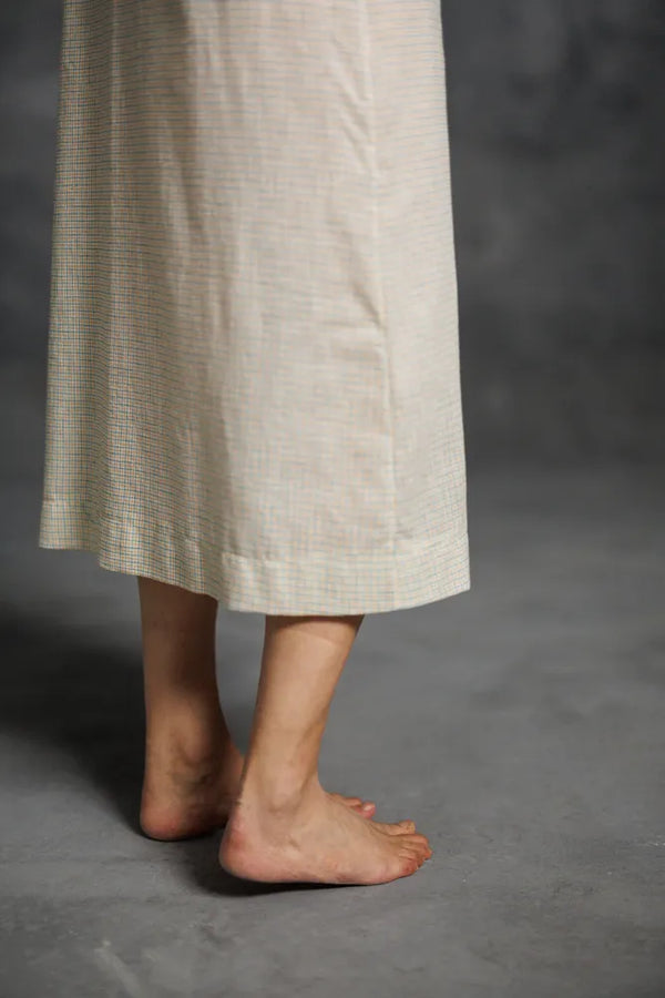 Person wearing a long beige dress made using The Lilian Sewing Pattern by Merchant & Mills with bare feet on a gray background