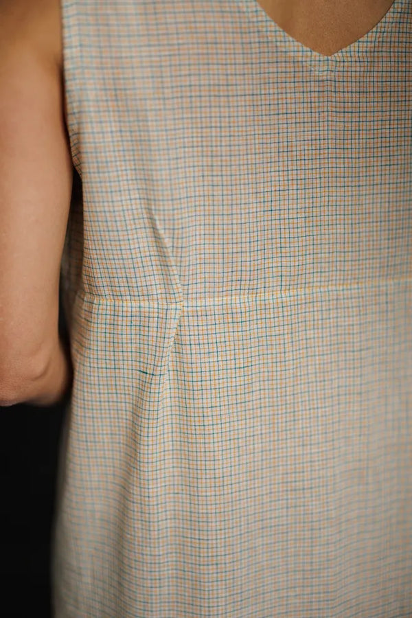 Close-up of a sleeveless checkered dress made using The Lilian Sewing Pattern by Merchant & Mills with a neutral background
