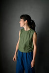 Woman wearing a green sleeveless top and blue The 101 Trouser Sewing Pattern by Merchant & Mills – relaxed drawstring linen trousers for beginners against a dark background