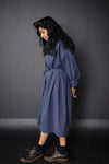 Woman wearing a blue The Cawley Sewing Pattern by Merchant & Mills against a dark gray background
