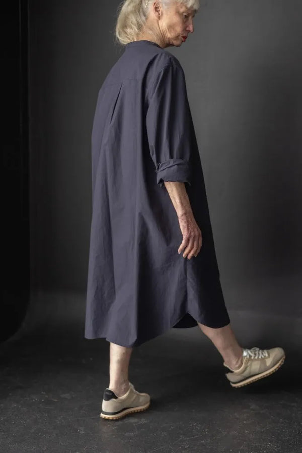 Person wearing a long dark blue dress made using The Niven Sewing Pattern by Merchant & Millsagainst a black background