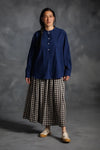 Person wearing a blue top made using The Niven Sewing Pattern by Merchant & Millsand checkered skirt against a gray background
