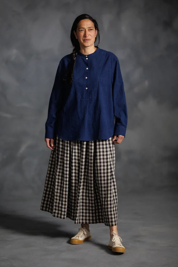 Person wearing a blue top made using The Niven Sewing Pattern by Merchant & Millsand checkered skirt against a gray background