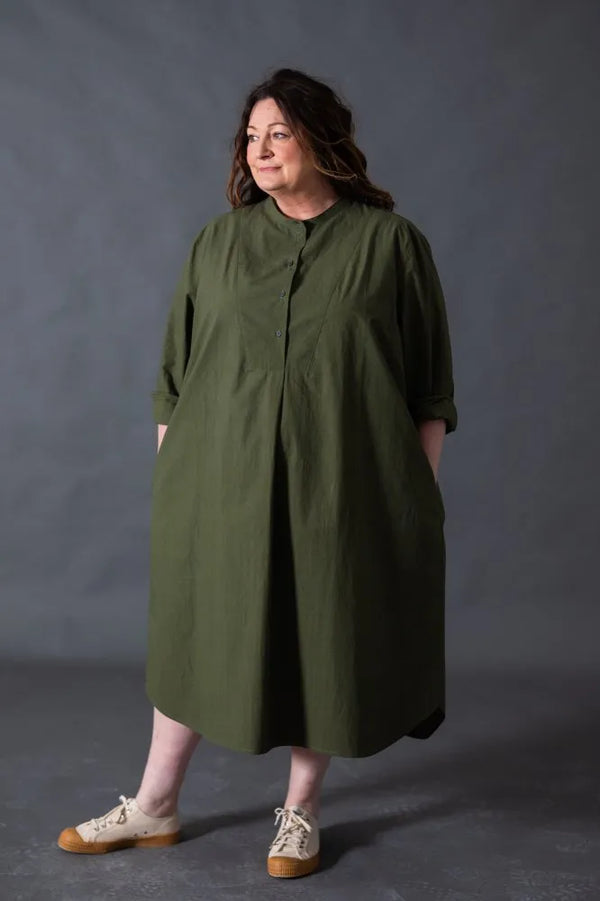 Woman wearing a green dress made using The Niven Sewing Pattern by Merchant & Millsagainst a gray background