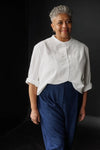 Person wearing a white blouse made using The Niven Sewing Pattern by Merchant & Mills and blue pants against a black background