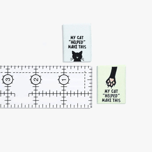 Two small signs with cat-themed text and a ruler for scale on a white background.