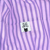 Close-up of a lavender and purple vertically striped fabric item with a small white sewn label that reads “MY CAT ‘HELPED’ MAKE THIS” above a black cat face graphic.