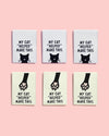 Six small rectangular canvas prints arranged in two rows on a light pink background. Each canvas features black text reading 'MY CAT "HELPED" MAKE THIS' with a black cat face or paw print on a white or cream background.