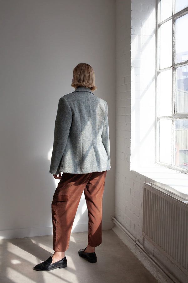 Person wearing a light blue jacket made using Naomi Blazer PDF Sewing Patternand brown pants standing in a room with a large window.