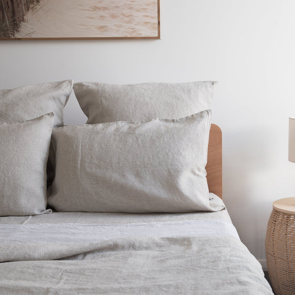 Neatly made bed with Natural linen pillowcases bedding and pillows in a bedroom setting.