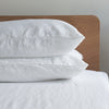 Pure white linenpillows on a bed with a wooden headboard against a neutral wall