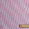 Red and white striped fabric with a wooden ruler for scale on a pink background