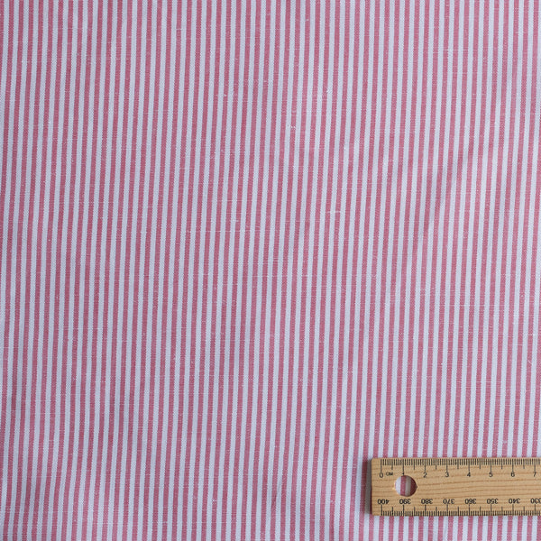 Red and white striped fabric with a wooden ruler for scale on a pink background