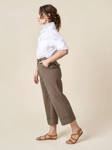 Woman wearing a white shirt and brown pantsmade of Rika Pants sewing pattern in cropped tailored style with hem cuffs and tabbed waistbandagainst a beige background