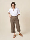 Person wearing a white shirt and brown pants made of Rika Pants sewing pattern in cropped tailored style with hem cuffs and tabbed waistbandon a beigebackground