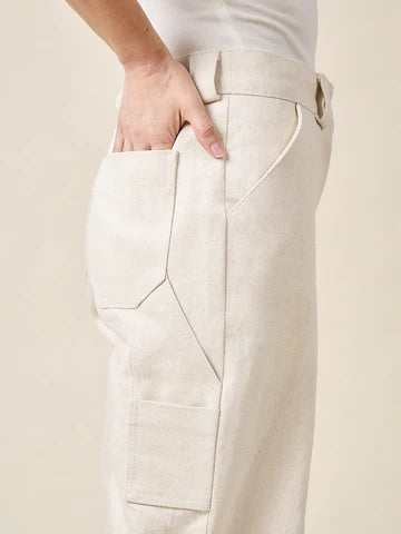Close-up of beige pants made of Rika Pants sewing pattern in cropped tailored style with hem cuffs and tabbed waistbandwith a plain background