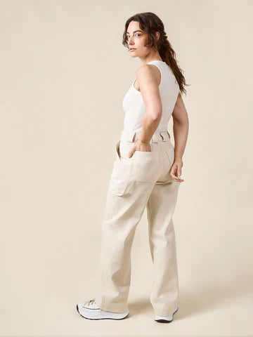 Woman wearing a white sleeveless top and beige pants against a plain background
