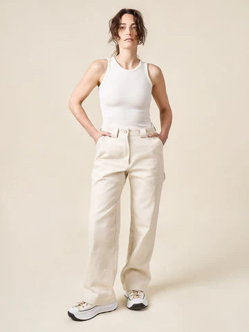 Woman wearing a white tank top and beige pants made of Rika Pants sewing pattern in cropped tailored style with hem cuffs and tabbed waistbandagainst a plain background