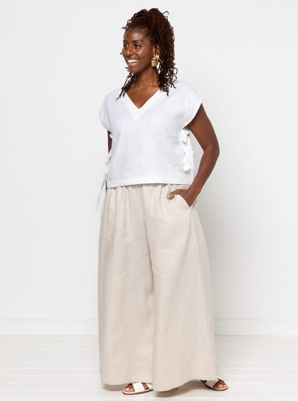 Woman wearing a white top and beige pants made using Rumi Top Sewing Pattern against a white background