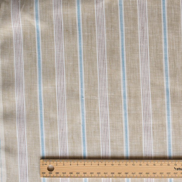 Seagrass Pinstripe linen fabric with pale sage-beige base, light-brown pinstripes, white and blue accents, 100% linen, 130 GSM, 60 LEA fabric with a ruler at the bottom for scale